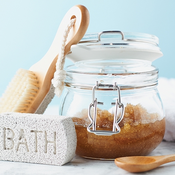 A DIY scrub made with sugar or salt in a glass container with bath tools
