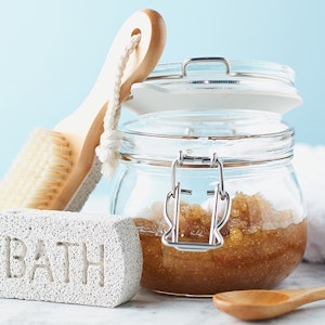 A DIY scrub made with sugar or salt in a glass container with bath tools
