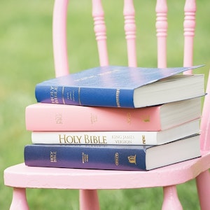 A stack of Bibles rests on a child's pink chair.
