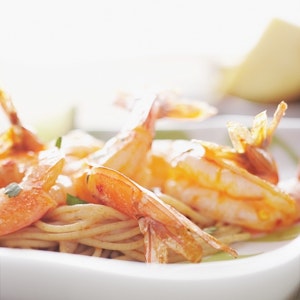 A portion of Chili-Lime Shrimp with pasta is served in a white dish.
