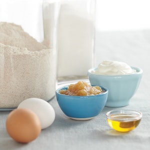 Flour, eggs, applesauce, honey, and Greek yogurt sit on a counter, waiting to be substituted for less healthy ingredients.
