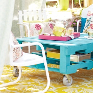 Chairs surround a bright outdoor table made from a pallet.
